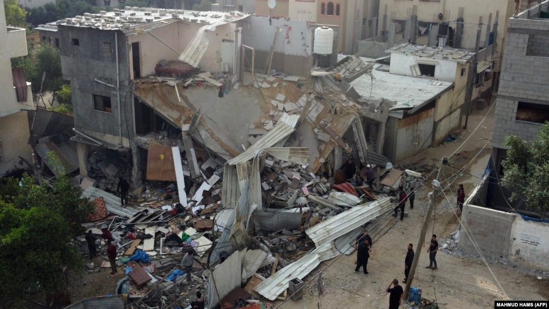 Orang-orang berkumpul di depan bangunan yang terkena serangan udara oleh Israel di Kota Gaza, Sabtu, 13 Mei 2023. Israel dan Gaza saling menembakan artileri berat pada 12 Mei, tetapi Mesir berhasil memediasi untuk menghentikan konflik. (Foto: Mahmud Hams/AFP)