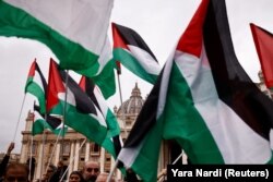 Orang-orang memegang bendera Palestina saat berkumpul untuk mendengarkan pesan tradisional Hari Natal Urbi et Orbi dari balkon utama Basilika Santo Petrus di Vatikan, 25 Desember 2023. (Foto: REUTERS/ Yara Nardi)