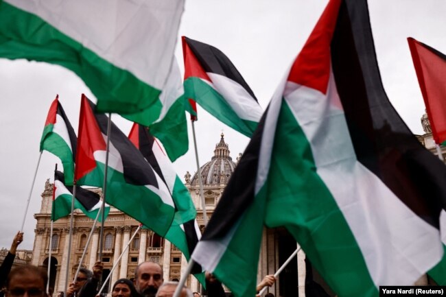 Orang-orang memegang bendera Palestina saat berkumpul untuk mendengarkan pesan tradisional Hari Natal Urbi et Orbi dari balkon utama Basilika Santo Petrus di Vatikan, 25 Desember 2023. (Foto: REUTERS/ Yara Nardi)