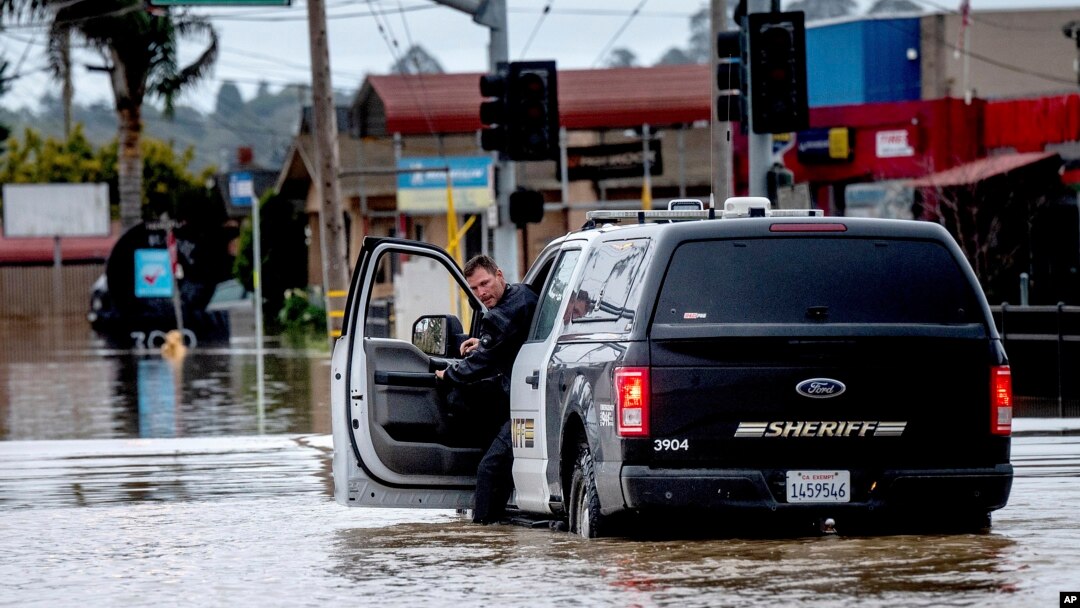 Seorang wakil sheriff mengecek kendaraannya saat melintasi jalan yang tergenang banjir di kawasan Pajaro, Monterey County, California, Senin, 13 Maret 2023. (Foto: Noah Berger/AP Photo)