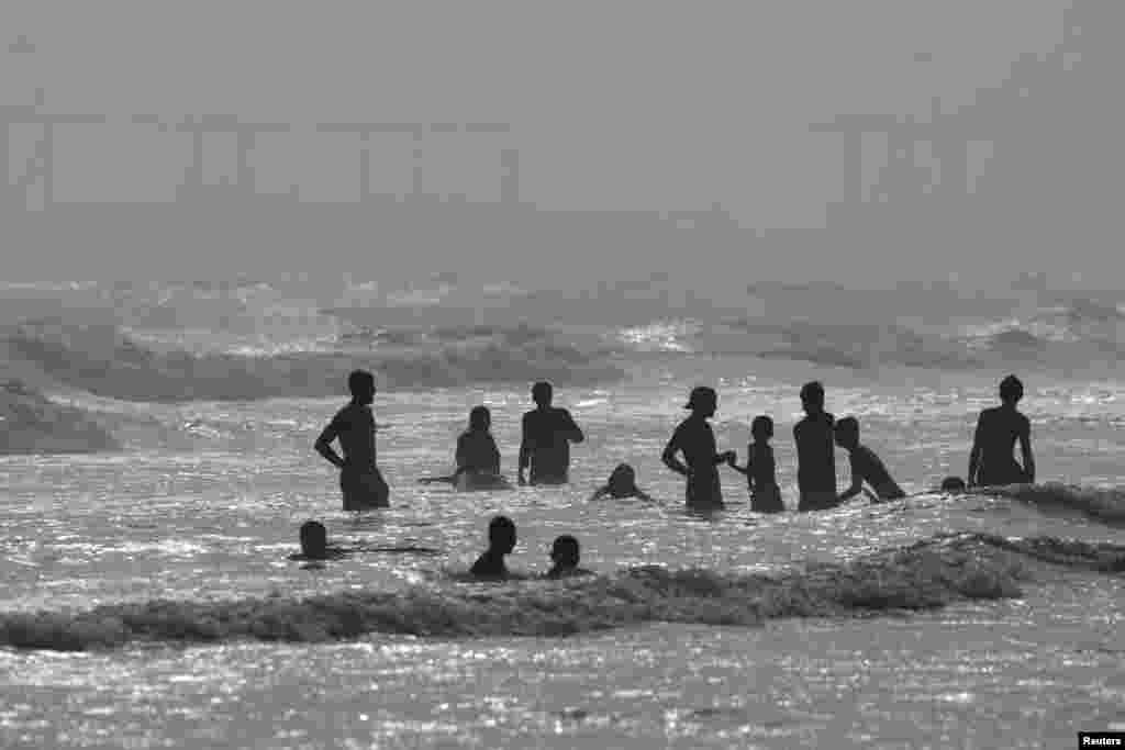 People are silhouetted as they take a bath in the Arabian Sea near Clifton Beach during a hot and humid day in Karachi, Pakistan, June 1, 2024. 