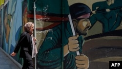 A woman walks past a mural depicting members of Iran's Revolutionary Guards at Tehran's Palestine square, Aug. 8, 2024. The Revolutionary Guards are holding military drills in the western parts of the country that will continue until Tuesday.