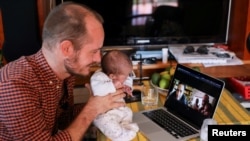 FILE - Namibian citizen Phillip Luhl holds one of his twin daughters as he speaks to his Mexican husband Guillermo Delgado via Zoom meeting in Johannesburg, South Africa, April 13, 2021.