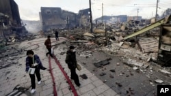 People walk past collapsed buildings following an earthquake in Wajima, Ishikawa prefecture, Japan Tuesday, Jan. 2, 2024. (Kyodo News via AP)