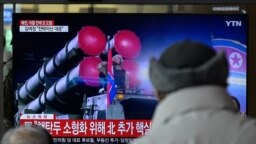 Men watch a television showing a news broadcast with file footage of a North Korean military parade, at a railway station in Seoul, Feb. 20, 2023. 