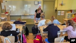 A teacher helps students practice their handwriting at the Djurgardsskolan elementary school in Stockholm, Sweden, Aug. 31, 2023. With summer vacations concluded, many teachers are putting a new emphasis on printed books, quiet reading hours, and practicing handwriting.