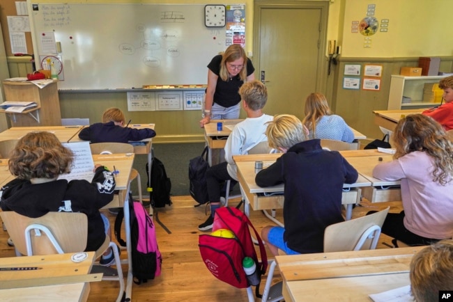 FILE - A teacher helps students practice their handwriting at the Djurgardsskolan elementary school in Stockholm, Sweden, Aug. 31, 2023. (AP Photo/David Keyton)