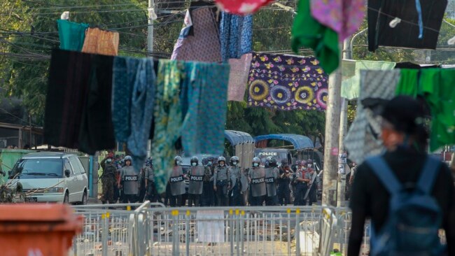 An anti-coup protester stands behind a line of women's clothing hung across a road to deter security personnel from closing in, in Yangon, Myanmar, March 9, 2021. In Burmese culture, walking under women's clothing is believed to weaken the power of men and bring bad fortune.