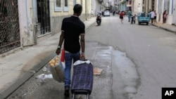 A man pulls a portable shopping cart while carrying a bag filled with bread, in Havana, Cuba, March 11, 2024.