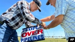 Gaylen Dewing, left, and Marvin Abraham affix a sign to a roadside fence east of Bismarck, N.D., Aug. 15, 2023.