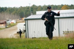 A police officer gives an order to the public during a manhunt at a farm for the suspect in this week's deadly mass shootings, Oct. 27, 2023, in Lisbon, Maine.