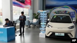 FILE - Staf penjualan berdiri di dekat kendaraan listrik Seagull buatan produsen mobil China BYD di ruang pamer di Beijing, 10 April 2024. (AP/Ng Han Guan)
