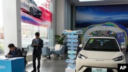 Tim marketing dari produsen mobil listrik BYD berdiri di dekat mobil listrik pabrikan tersebut di sebuah showroom di Beijing, pada 10 April 2024. (Foto: AP/Ng Han Guan)
