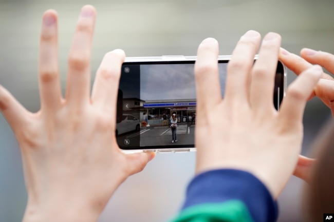 Tourists take a photo of the Lawson convenience store with Mt. Fuji in the background on cloudy evening of Tuesday, April 30, 2024, at Fujikawaguchiko town, in central Japan. (AP Photo/Eugene Hoshiko)