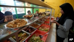 A worker serves customers at a food stall in Bekasi, on the outskirts of Jakarta, Indonesia, Thursday, Feb 2, 2023. (AP Photo/Achmad Ibrahim)