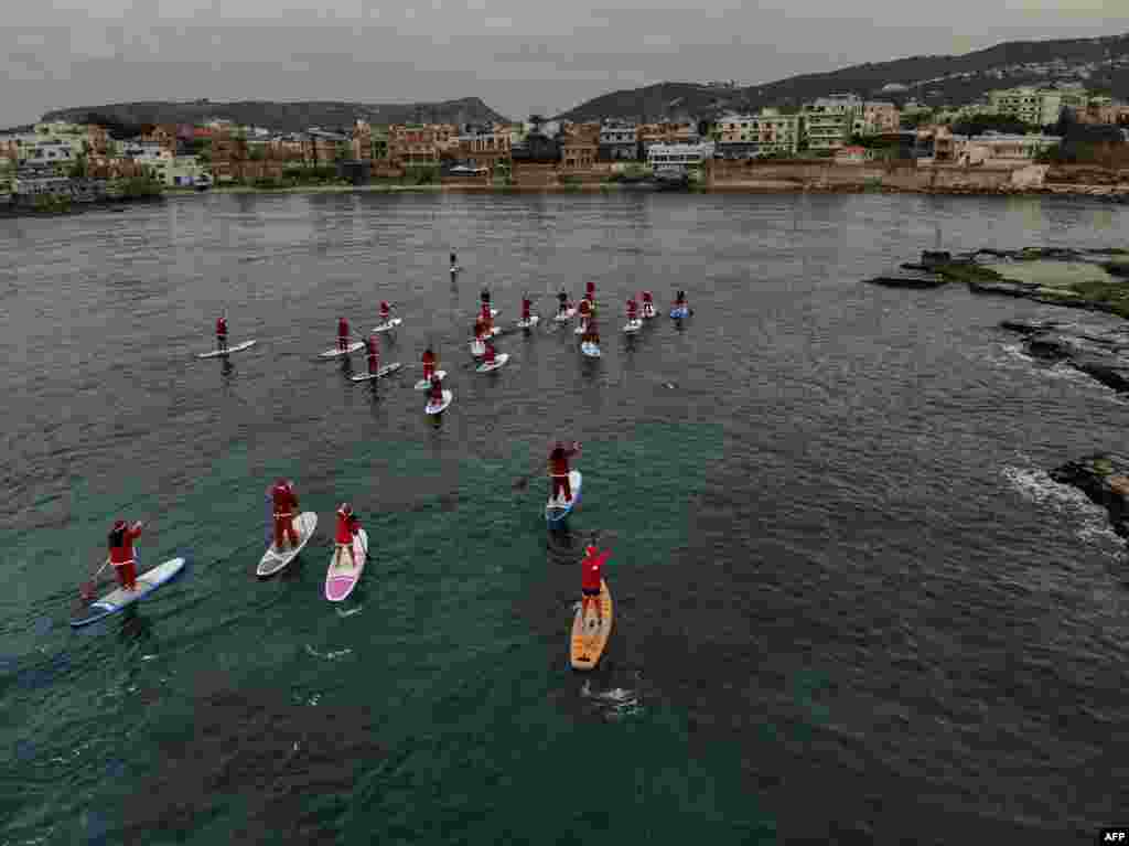 People dressed in Santa Claus outfits riding on standup paddles in the Mediterranean Sea, in Lebanon&#39;s northern coastal city of Batroun, Lebanon.