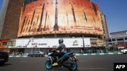 Un hombre pasa en motocicleta junto a un cartel que muestra misiles balísticos iraníes en servicio en Teherán el 19 de abril de 2024.