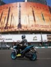 A man rides a motorbike past a billboard depicting Iranian ballistic missiles in service in Tehran on April 19, 2024. 