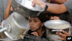 Um rapaz palestiniano espera pela sua porção de ajuda alimentar antes a 15 de junho de 2024.