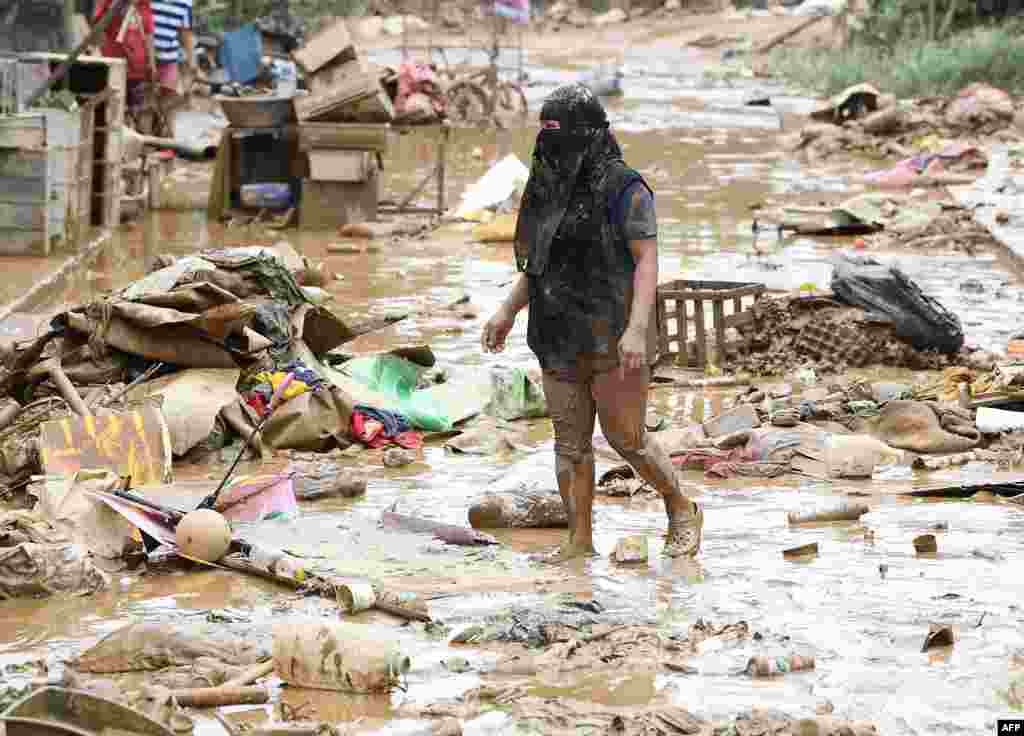 A resident walks amongst debris of destroyed belongings next to her house at a village in Manila, July 25, 2024, a day after heavy rains fueled by Typhoon Gaemi and the seasonal monsoon lashed Manila and surrounding regions.