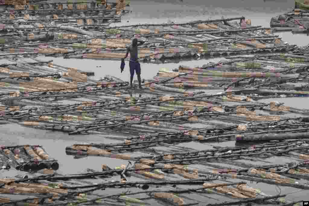 Seorang pria berjalan melintasi rakit-rakit kayu di kota Lagos, Nigeria.