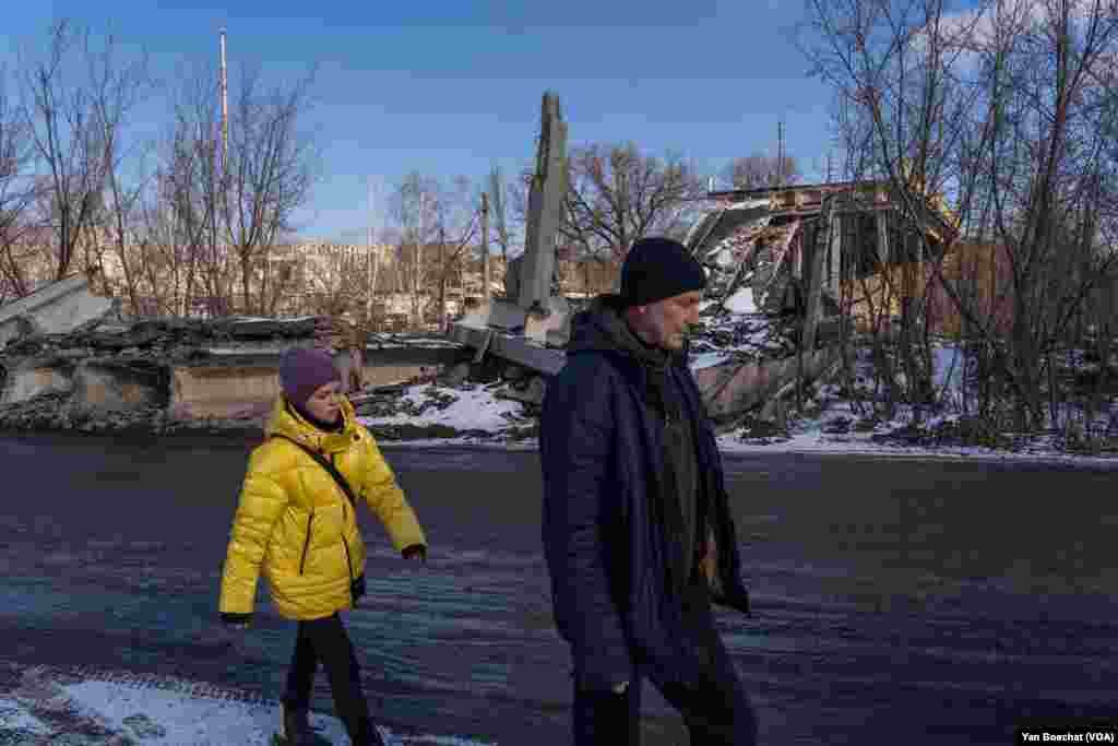 A man and a young girl walk by one of the many bridges destroyed in Kupiansk, Feb. 17, 2023.