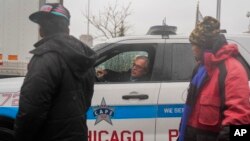Citing safety concerns about migrants crossing the street in traffic, a Chicago police officer instructs a pastor leading them to tell people to meet him down the street where "warming" buses are parked, Jan. 12, 2024, in Chicago.