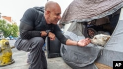 Dr. Kwane Stewart approaches the dog Popcorn protecting his owner's tent in the Skid Row area of Los Angeles on June 7, 2023.