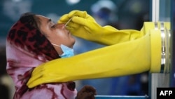 বাংলাদেশের ঢাকায় করোনভাইরাস পরীক্ষা করতে আসা একজন মহিলার কাছ থেকে সোয়াব নমুনা সংগ্রহ করছেন মুগদা মেডিকেল কলেজ ও হাসপাতালের একজন কর্মচারী। ১৭ জুন, ২০২০। (ফাইল ছবি) , 