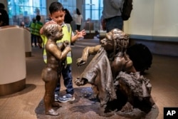 A boy pats the head of a sculpture of a Neanderthal boy, inside the Smithsonian Hall of Human Origins, July 20, 2023, at the Smithsonian Museum of Natural History in Washington.