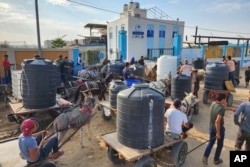 Palestinians queue to collect drinking water from a water treatment station in the central Gaza Strip to distribute to displaced people at the U.N. school shelters in Deir al Balah, Gaza Strip, Oct. 27, 2023.