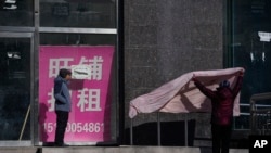 北京街头一名女子在一家空置招租店铺外晒被子。（2023年12月17日）