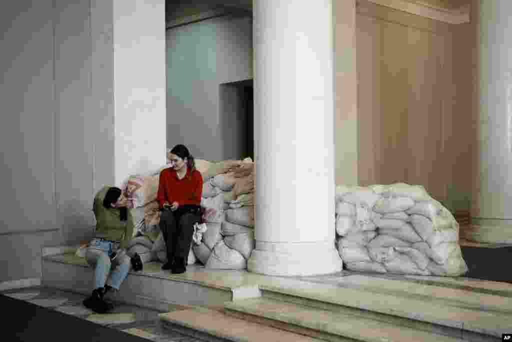 Dos reporteras, sentadas sobre sacos de arena en el interior de un edificio en Kiev, Ucrania, el 27 de febrero de 2023. Hay sacos de arena protegiendo estatuas y barreras antitanque en las calles, trincheras en los bosques cercanos y avisos de minas terrestres en el monte. Las señales pintadas en las paredes indican el refugio más próximo, mientras las sirenas antiaéreas suenan ocasionalmente en la ciudad, que a veces sufre ataques con misiles.&nbsp;