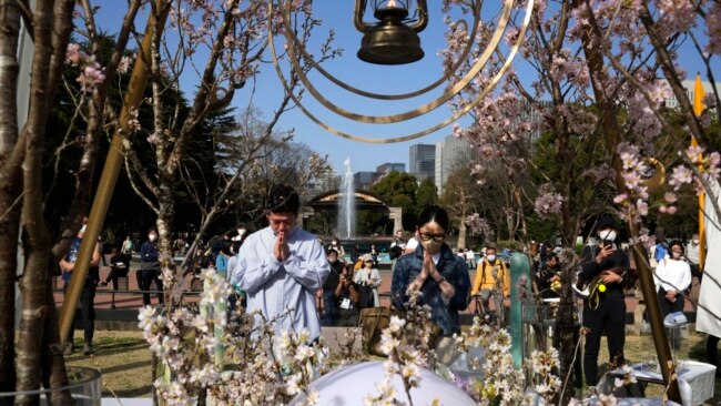 A man and a woman pray after laying flowers in front of a memorial marking the 12th anniversary of the massive earthquake, tsunami and nuclear disaster, at Hibiya Park in Tokyo, March 11, 2023.