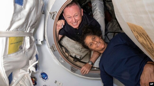 In this photo provided by NASA, Boeing Crew Flight Test astronauts Butch Wilmore, left, and Suni Williams pose inside the International Space Station's Harmony module and Boeing's Starliner spacecraft on June 13, 2024. (NASA via AP)