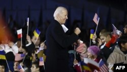 Presiden AS Joe Biden berdiri di tengah anak-anak yang bersorak dengan mengibarkan bendera AS, Polandia, dan Ukraina setelah menyampaikan pidato di depan Royal Warsaw Castle Gardens di Warsawa, Polandia pada 21 Februari 2023. (Foto: AFP)
