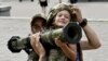 A Ukrainian serviceman helps a boy wearing body armor to hold an AT4 Swedish man-portable anti-tank weapon at a volunteers point in the center of Kyiv on Aug. 10, 2023.