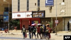 FILE - People carrying their belongings walk along a street in Khartoum on April 16, 2023, as fighting between the forces of 2 rival generals continues.