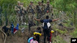 Un migrant parle aux gardes nationaux texans qui se tiennent derrière des barbelés sur la rive du Rio Grande, vu de Matamoros, au Mexique, le 11 mai 2023. 