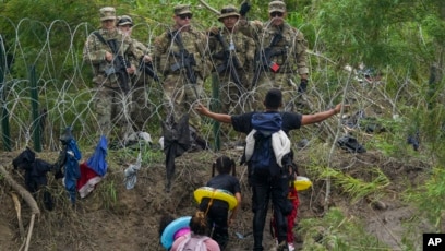 Un migrant parle aux gardes nationaux texans qui se tiennent derrière des barbelés sur la rive du Rio Grande, vu de Matamoros, au Mexique, le 11 mai 2023. 