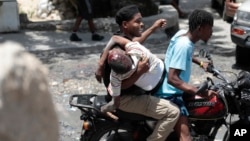 FILE - A police officer holds onto a man injured during gang clashes, as they are driven away on the back of a moto-taxi, in Port-au-Prince, Haiti, Aug. 15, 2023.