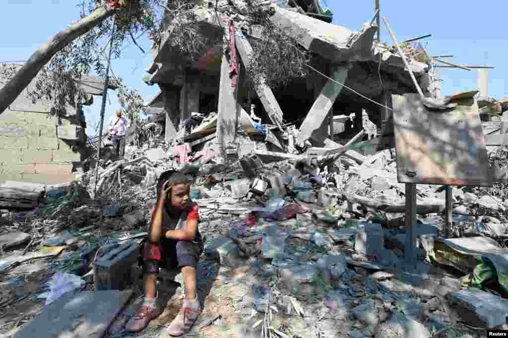 A child sits amid the rubble as Palestinians inspect a house destroyed in an Israeli strike, amid the Israel-Hamas conflict, in Nusairat refuge camp, in the central Gaza Strip.