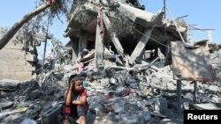 Un enfant est assis au milieu des décombres alors que les Palestiniens inspectent une maison détruite par une frappe israélienne, dans le cadre du conflit entre Israël et le Hamas, dans le camp de réfugiés de Nusairat, dans le centre de la bande de Gaza, le 9 juillet 2024.