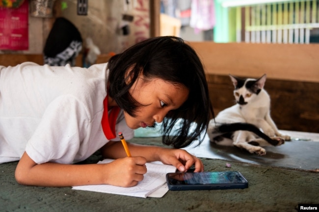 FILE - A student answers her learning module following the suspension of in-person classes, at her family's empty store, in Manila, Philippines, April 26, 2024. (REUTERS/Lisa Marie David)