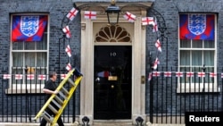 A worker carries a ladder past England bunting and flags outside 10 Downing Street in London on Aug. 18, 2023, ahead of England playing against Spain on Sunday in the final of the Women's World Cup. 