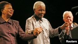 FILE - Former president of South Africa, Nelson Mandela (C) is escorted by his wife Graca Machel (L) and former U.S. President Jimmy Carter (R) during a ceremony marking his 89th birthday in Johannesburg, July 18, 2007. 