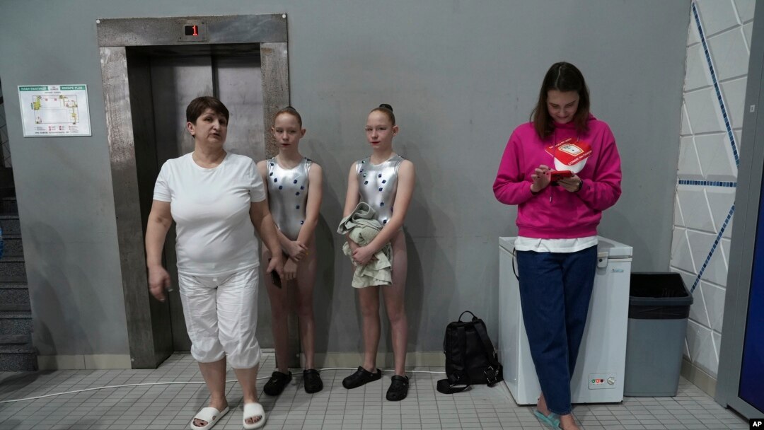 A pair of competitors wait with officials on the sidelines of the Ukrainian national artistic swimming championships in Kyiv, Ukraine, on Feb. 18, 2023.