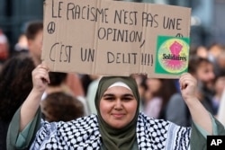 FILE - A woman holds a sign that reads in French, '"Racism is not an opinion, it is a crime," as she waits for the results of the second round of legislative elections, July 7, 2024, in Nantes, western France.