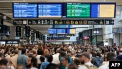 Passengers gather around the departure and arrival boards at the Gare Montparnasse train station in Paris on July 26, 2024 as France's high-speed rail network was hit by malicious acts disrupting the transport system.