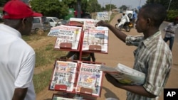 FILE - A newspaper vendor, right, shows papers to a potential buyer, left, in Ggabe, near Kampala, in Uganda, Feb. 19, 2016. 